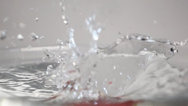 Three Fresh tasty red strawberries dropping down into the transparent water with stuning splashes breaking the liquid surface on the white background isolated. Shot on high-speed camera in slow motion
