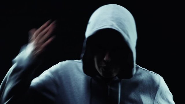 Slow motion of an angry hooded tomboy gesturing against a black background

