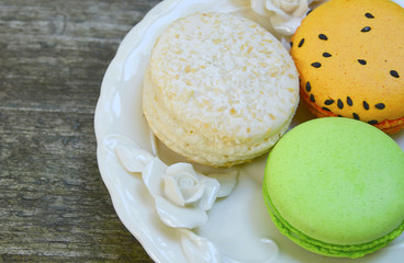 Colorful french macarons on decorative plate on old wooden table.