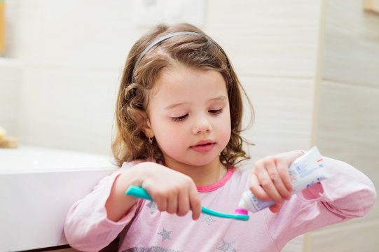 Little girl in bathroom putting a toothpaste on toothbrush