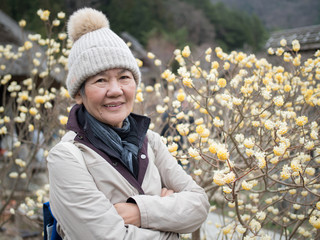 Senior Asian woman looking and smiling to the camera. Background is yellow flower.