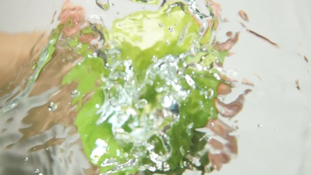 Man hand reaches and grabs green fresh tasty apple floating in water super slow motion shot. White background isolated shot. Underwater camera up vertical view