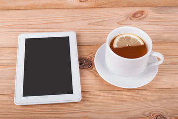 Obraz na płótnie Canvas Tea with lemon and tablet computer on a wooden table.