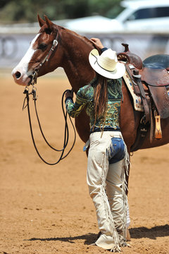 The western style rider with cowboy chaps and hat is caring for her horse
