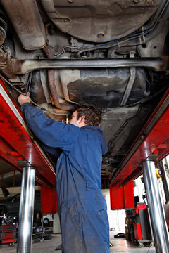 car mechanic in workwear is standing under a car