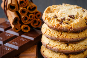 Chocolate cookies stacked vertical, milk and dark chocolate bar and cinnamon on rustic wooden...