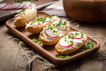 Toasts with radish, chives and cottage cheese on a wooden table.