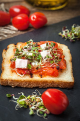 Grilled toasted bread with roasted tomatoes, feta cheese and radish sprouts.
