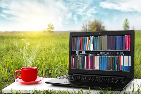 Laptop and cup of hot coffee on the background picturesque nature, outdoor office. E-book library concept with laptop computer and book. Old books on a wooden shelf. Travel concept. Business ideas.