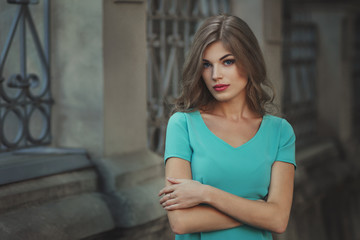 Outdoor lifestyle portrait of pretty young girl, wearing in blue dress on urban background. Creative color toned image.