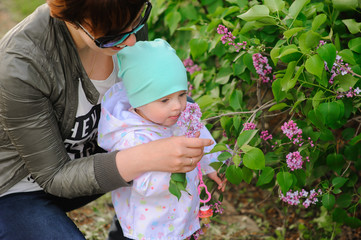 Happy mother and daughter in the garden of blooming lilacs