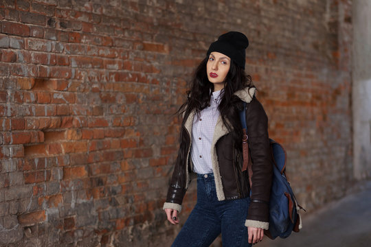 Outdoor lifestyle portrait of pretty young girl, wearing hipster swag grunge style on urban background. Wearing hat and jeans with backpack. Spring fashion woman. Toned style instagram filters.