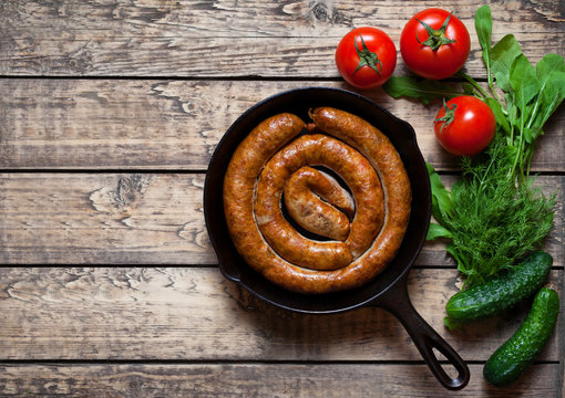 Meat sausage homemade roasted barbecue meal with tomatoes cucumbers and herbs on vintage wooden table background