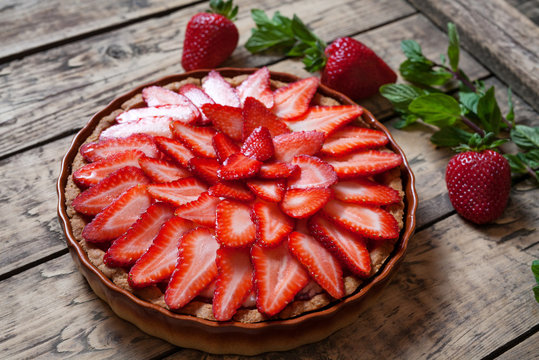 Homemade traditional strawberry tart with mint leaves on vintage wooden background