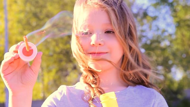маленькая девочка пускает мыльные пузыри на ветру