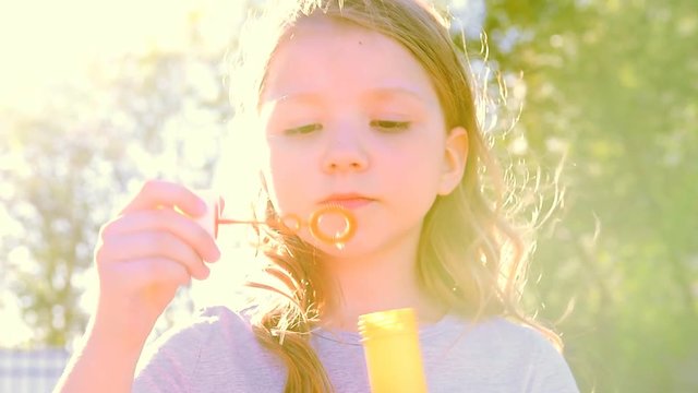 девочка пускает мыльные пузыри на ярком закатном солнце