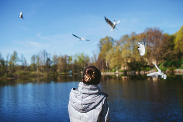 Girl stands with his back by the lake and watch the birds