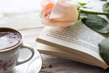 Turkish coffee with peach-colored rose, slices of chocolate and book on the wooden table 