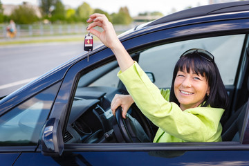 Happy smiling brunette woman Showing Car Key sitting in car with spring-summer mood. Dressed in green jacket with sun glasses on head. Woman Driving