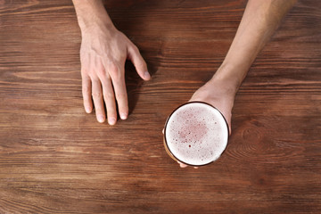 Male hand holding glass of beer on wooden background