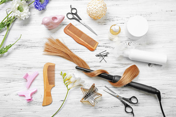 Fototapeta na wymiar Strand of hair with flowers, barber equipment and tools on light wooden background