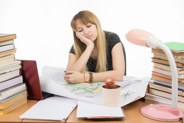 A girl student at a table with a pile of books, drawings and projects sitting sadly leaning on hand and eyes closed