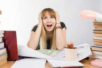 Girl design student at a desk with a pile of books and projects in desperation grabbed the head
