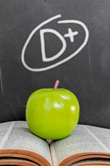 Green apple on old  open book over grade d plus on black chalkbo