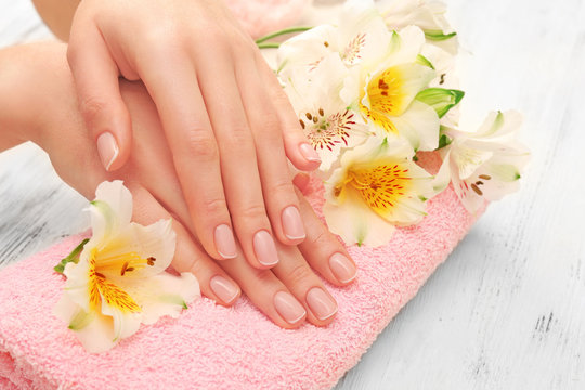 Spa concept. Woman hands with beautiful manicure and flowers on towel, close up