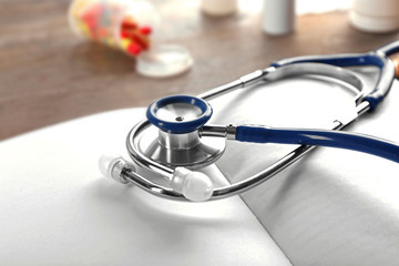 Stethoscope with open book and pills on wooden background. Medical literature concept