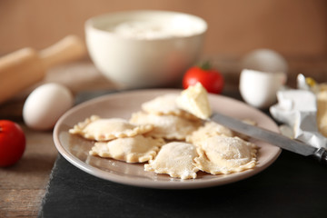 Uncooked ravioli on plate on wooden table