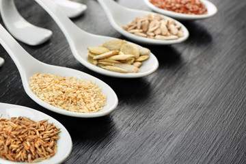 Different kinds of seeds in spoons on wooden table