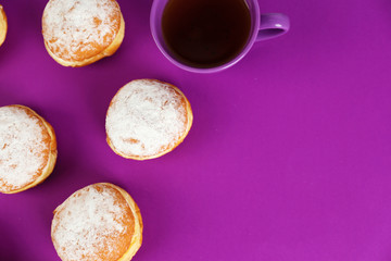 Delicious donuts with powdered sugar and cup of tea on purple surface, top view