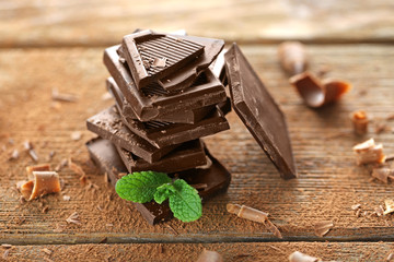 Stack of black chocolate pieces with fresh mint on wooden table