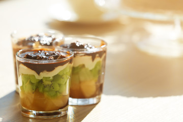 Fruits in glasses with whipped cream and chocolate syrup.