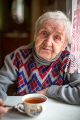 An old woman sitting in the kitchen drinking tea.