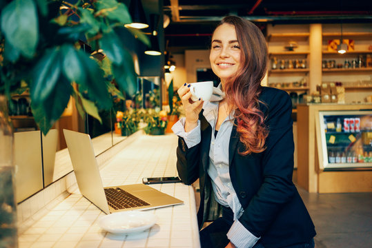 Portrait of a cute girl who is drinking morning coffee and enjoying a drink smiling. attractive female freelancer working with a laptop computer and drinking coffee in a coffee shop.