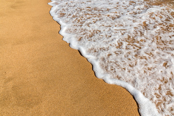 A small wave flows over a tropical sandy beach.