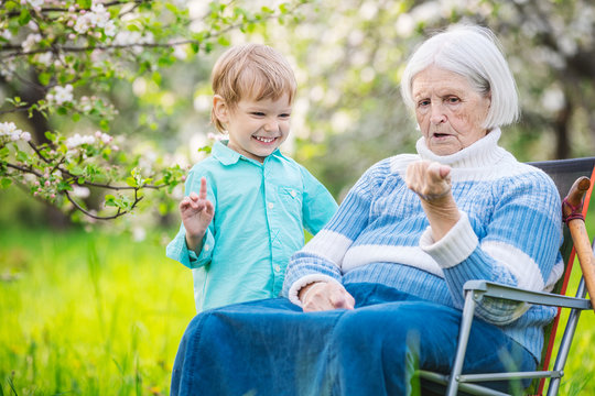 Senior woman showing something in hand to great grandson while relaxing in blossoming orchard