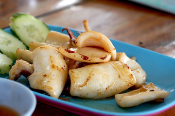 Grilled squid in blue plate on wood table ready to eat.
