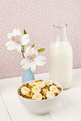 bowl of cereal with banana,  bottle of milk and flower