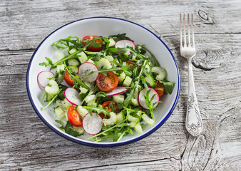 Fresh vegetable salad with cherry tomatoes, cucumbers, radishes and arugula. Healthy vegetarian food. On a light wooden rustic background