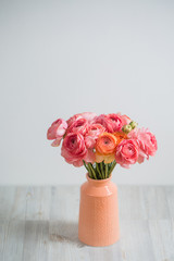 bunch of pale pink ranunculus persian buttercup  light background, wooden surface. glass vase