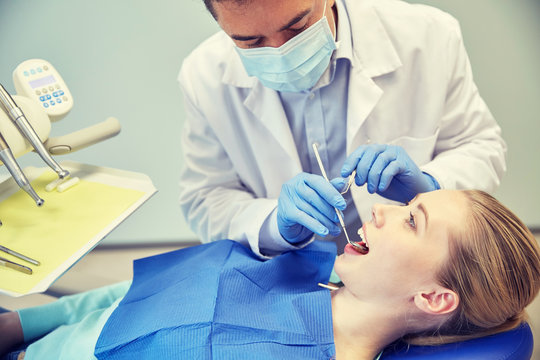 male dentist in mask checking female patient teeth