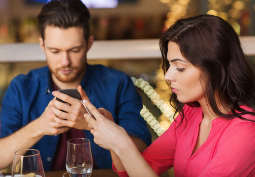 couple with smartphones dining at restaurant