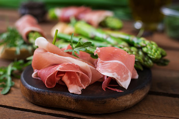 Parma ham, asparagus and arugula on a wooden background