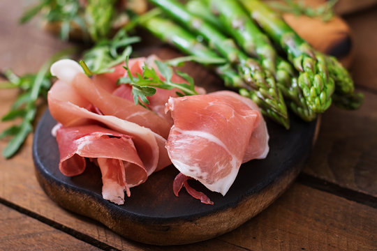 Fototapeta Parma ham, asparagus and arugula on a wooden background