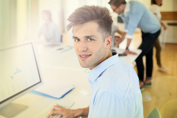 Office worker sitting in front of desktop, colleagues in background