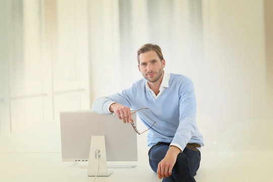 Businessman sitting on table by computer in modern room
