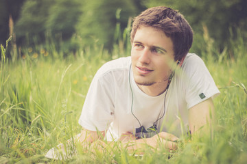 Naklejka na ściany i meble Junger Mann liegt im Gras und hört Musik